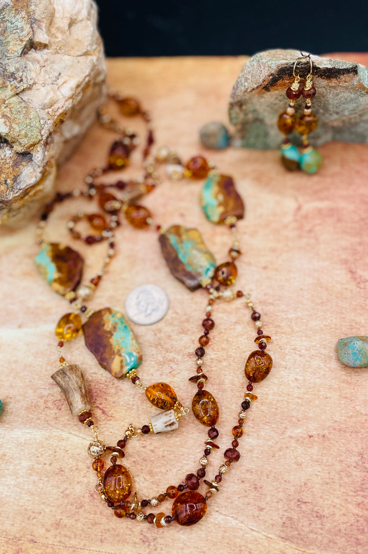 Extra long silk knotted and wire wrapped treasure necklace featuring Baltic amber, Kingman turquoise, garnets, and deer antlers with matching earrings and a U.S. quarter for size reference. Available only from Rockstar Cowgirl online or in store n Cody, Wyoming.