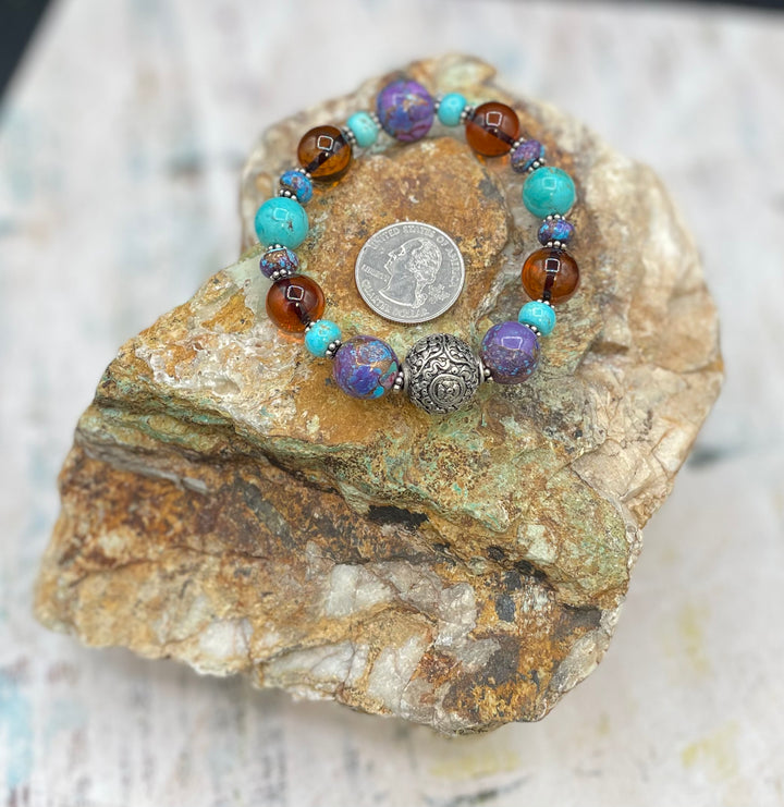 Close up of the bracelet. Features a sterling silver focal bead surrounded by purple Mojave and Kingman turquoise and Baltic amber beads.