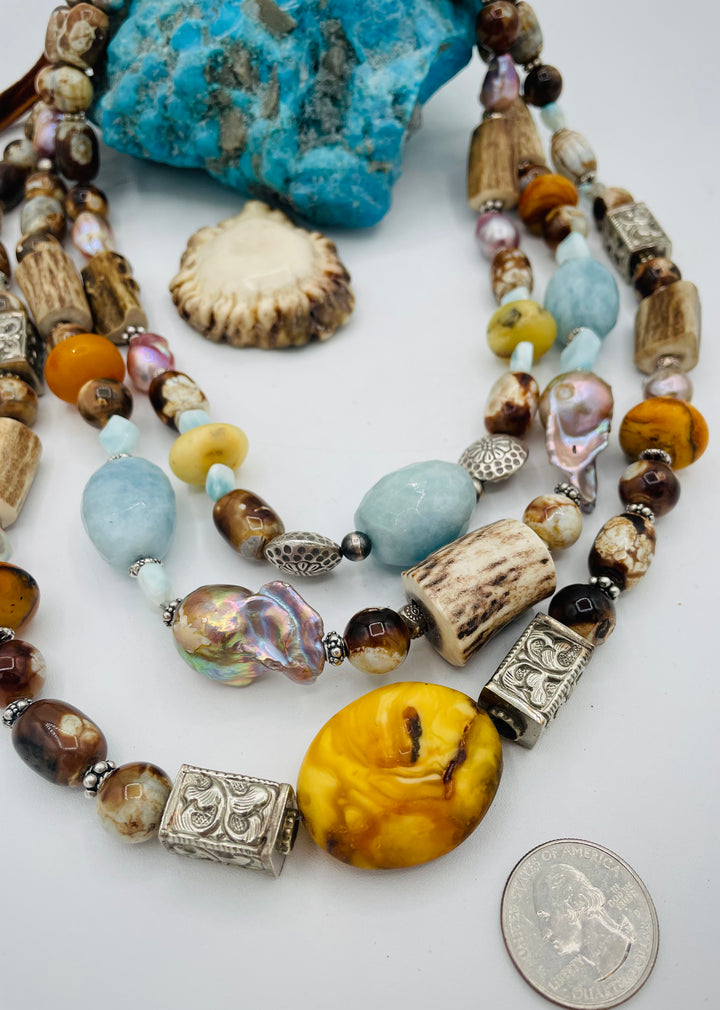 Chunky 3 strand beaded necklace featuring Baltic amber, baroque natural luster pearls, deer antler, larimar, aquamarine, wood opal, silver repousse beads, and sterling silver. U.S. quarter for size reference. Available only from Rockstar Cowgirl online or in store in  Cody, Wyoming.