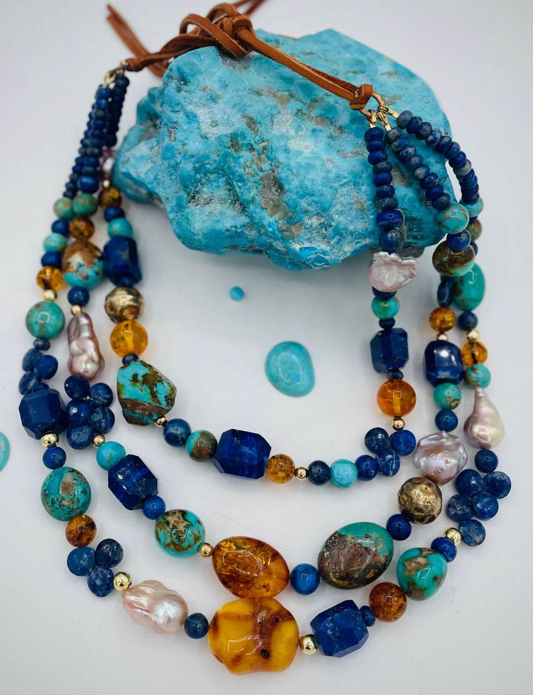Beaded 3 strand necklace featuring lapis, Baltic amber, Kingman turquoise, 14K gold beads, natural luster pearls, and finished with deer lace in the back. Available only form Rockstar Cowgirl online or in store in Cody, Wyoming.