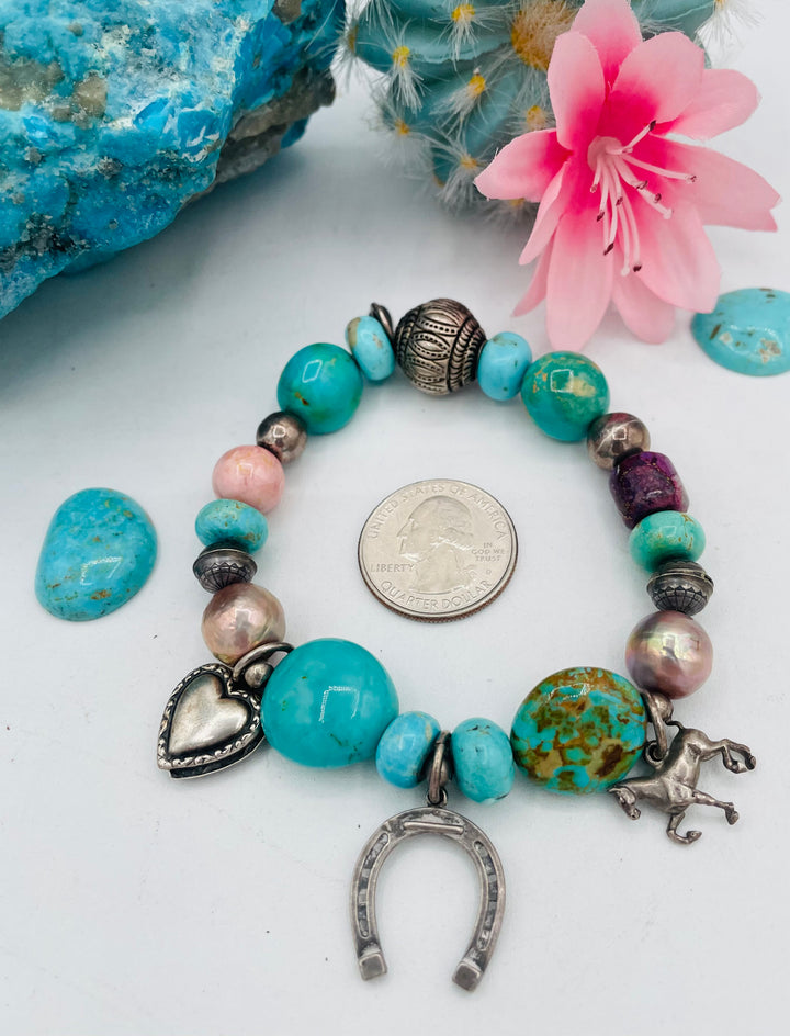 Beaded stretch bracelet featuring Kingman turquoise, royal beauty turquoise, pearls, rhodochrosite, purple turquoise, sterling silver beads and vintage sterling silver charms. U.S. quarter for size reference. Available only from Rockstar Cowgirl online or in store in Cody, Wyoming.