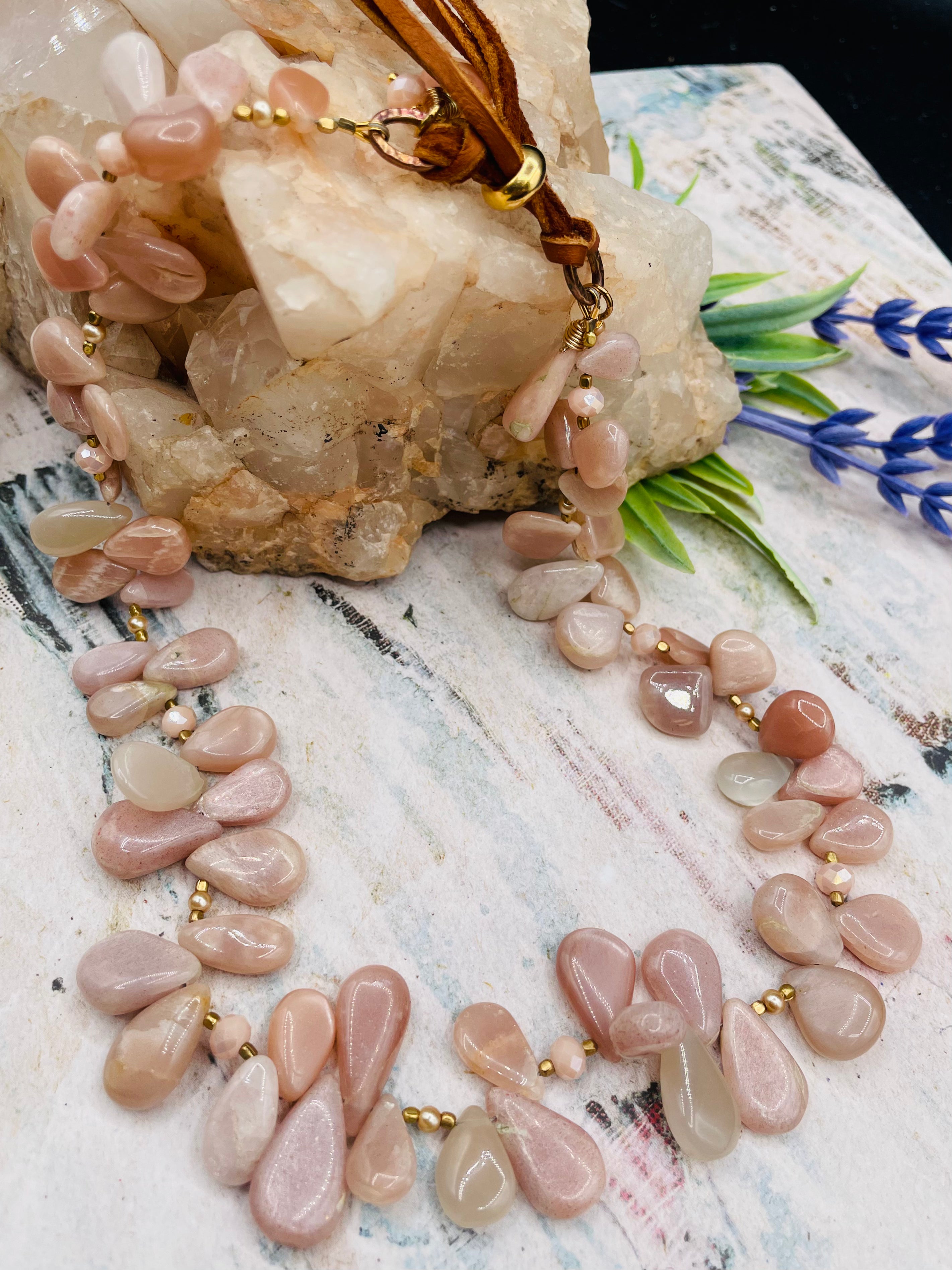 Creamy sunstone hatband or necklace with glass pearls, mauve crystals, and bronze sprinkled throughout finished with gold painted feathers, deer lace and slide bead for fit. Available only from Rockstar Cowgirl online or in store in Cody, Wyoming.