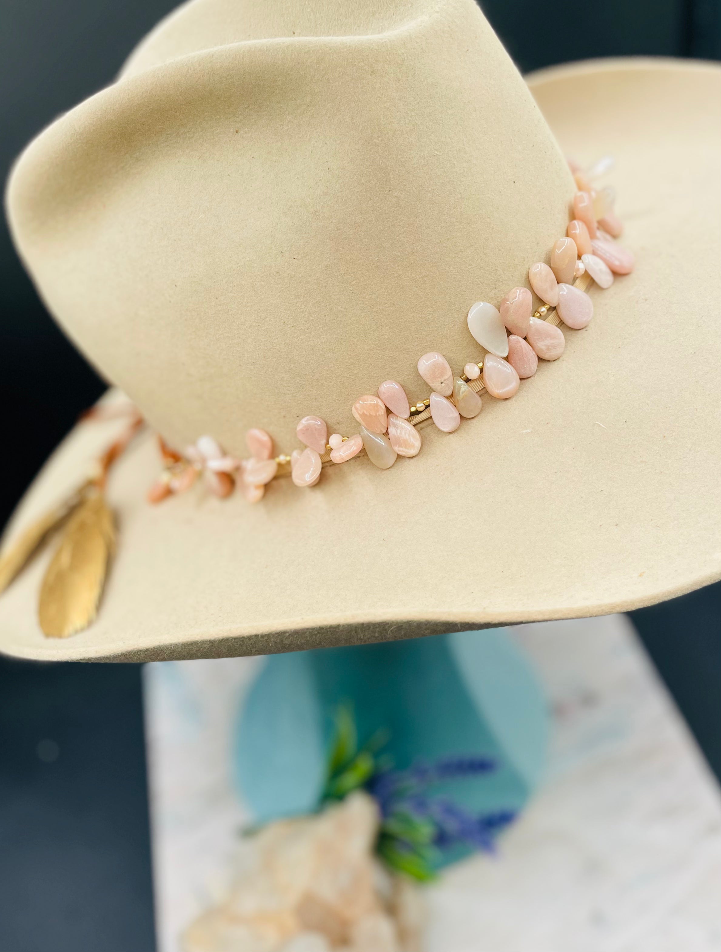 Creamy sunstone hatband or necklace with glass pearls, mauve crystals, and bronze sprinkled throughout finished with gold painted feathers, deer lace and slide bead for fit. Available only from Rockstar Cowgirl online or in store in Cody, Wyoming.