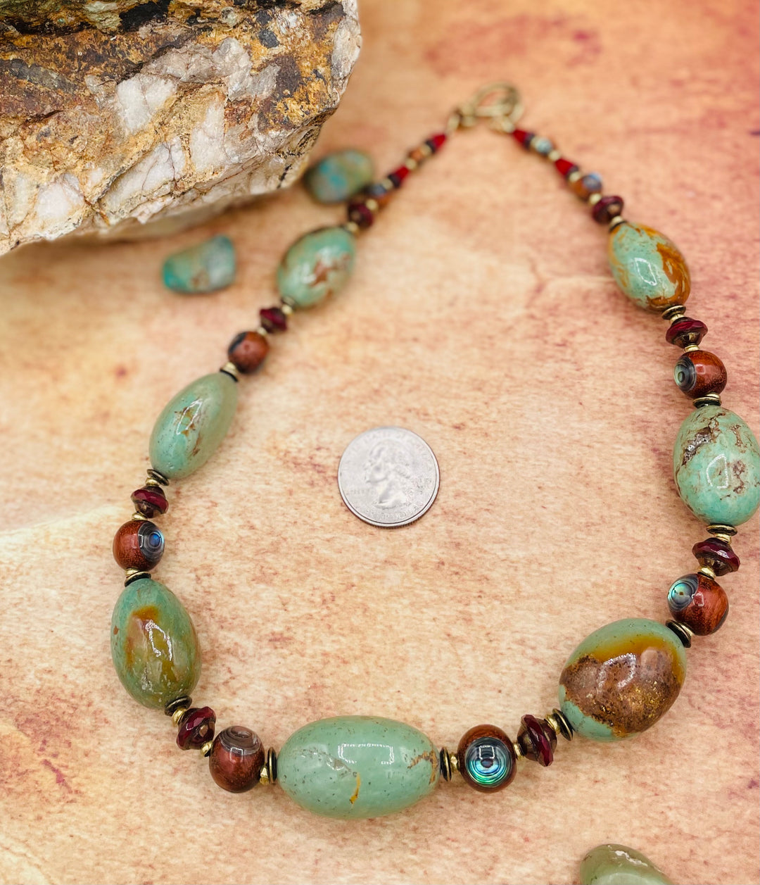 A necklace featuring large green Kingman turquoise nuggets, abalone inlaid wood beads, red Czech travertine beads, and brass. A U.S. quarter for a size reference. Available only from Rockstar Cowgirl online or in store in Cody, Wyoming.
