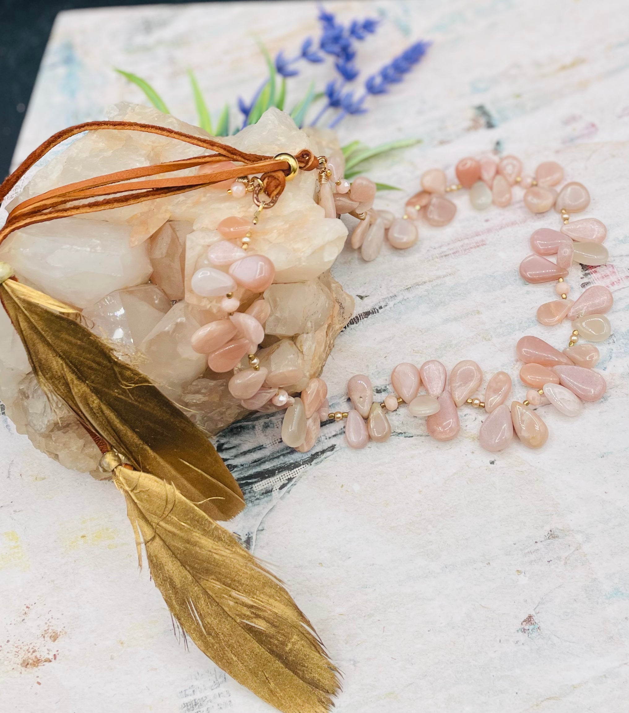 Creamy sunstone hatband or necklace with glass pearls, mauve crystals, and bronze sprinkled throughout finished with gold painted feathers, deer lace and slide bead for fit. Available only from Rockstar Cowgirl online or in store in Cody, Wyoming.