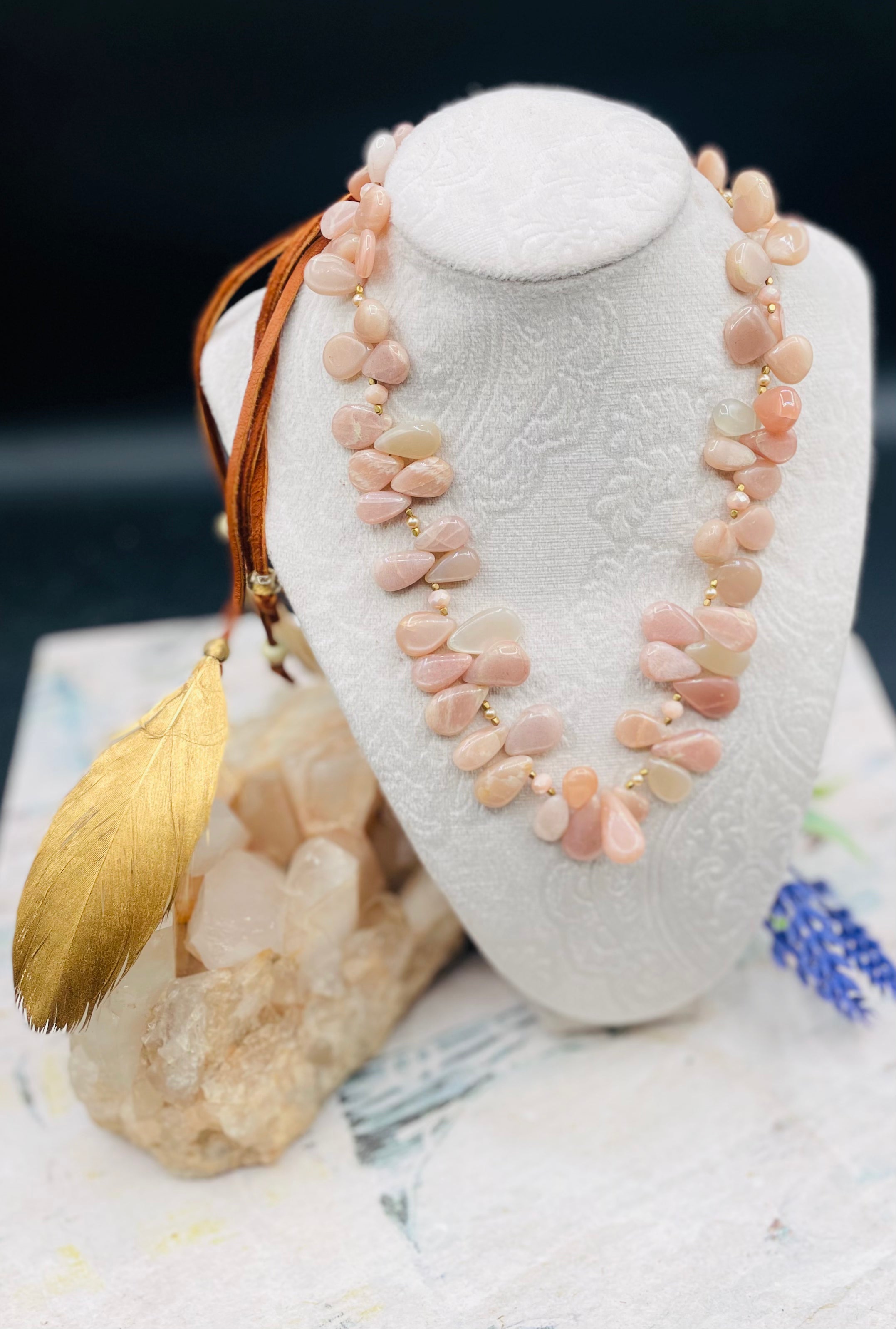 Creamy sunstone hatband or necklace with glass pearls, mauve crystals, and bronze sprinkled throughout finished with gold painted feathers, deer lace and slide bead for fit. Available only from Rockstar Cowgirl online or in store in Cody, Wyoming.